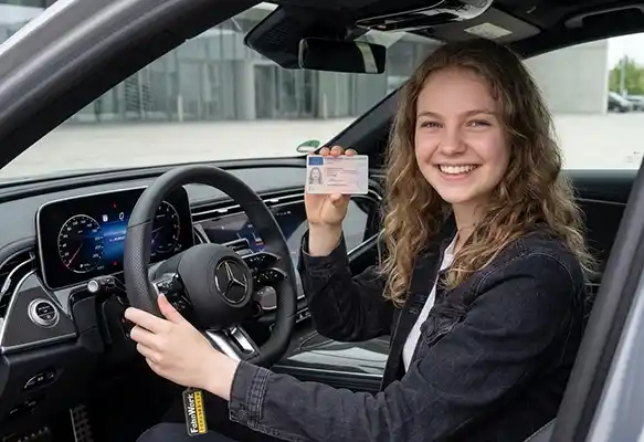 Schülerin der Fahrschule Darmstadt; FahrWerk lächelt auf dem Fahrersitz eines Mercedes und hält stolz ihren neuen EU-Führerschein in die Kamera.